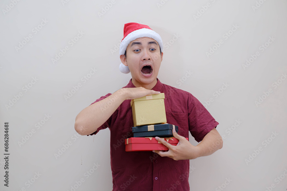 Young Asian Santa man drops Christmas boxes with shocked face expression and looking at the camera. Isolated beige background. Christmas Concept. Young Asian Santa man drops Christmas boxes with shocked face expression and looking at the camera. Isolated beige background. Christmas Concept.