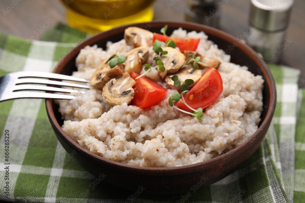 Delicious barley porridge with mushrooms, tomatoes and microgreens in bowl served on table, closeup Delicious barley porridge with mushrooms, tomatoes and microgreens in bowl served on table, closeup
