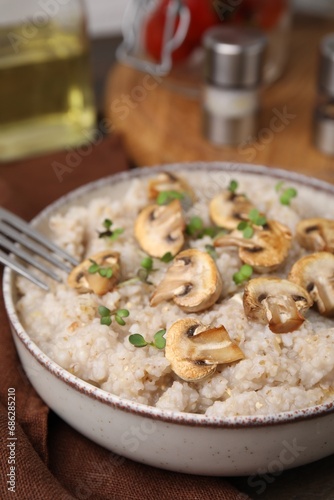 Delicious barley porridge with mushrooms and microgreens in bowl on table, closeup
