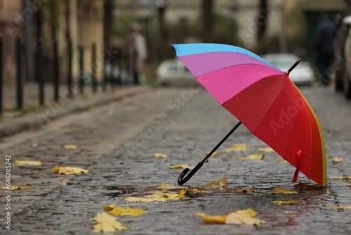 Fototapeta Naklejka Na Ścianę i Meble -  Open colorful umbrella and fallen leaves on city street. Space for text