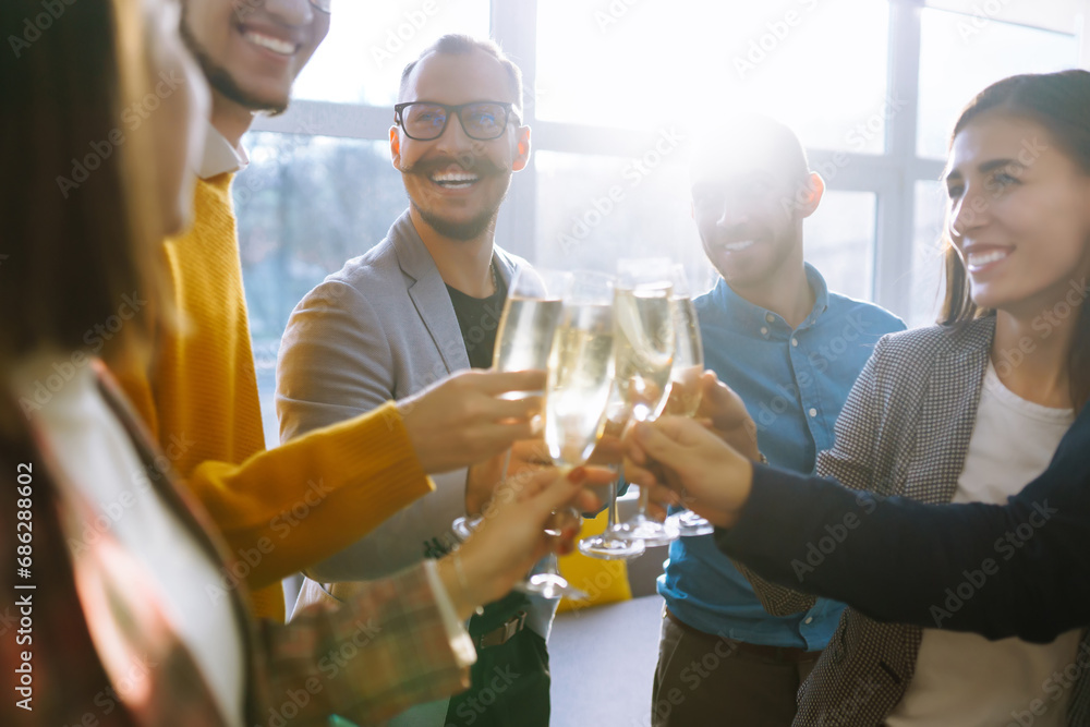 Business people celebrate with glasses of champagne in the office at a corporate event. A group of young people are having fun in the office. Holidays, business concept. - obrazy, fototapety, plakaty 