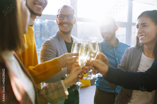 Business people celebrate with glasses of champagne in the office at a corporate event. A group of young people are having fun in the office. Holidays, business concept.