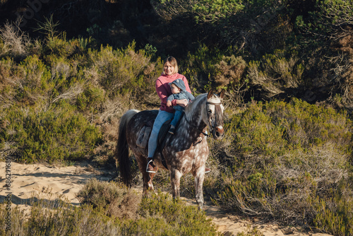 Happy mother riding spotted horse with little child