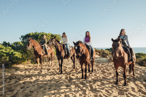 Female friends riding horses near bushes and sea
