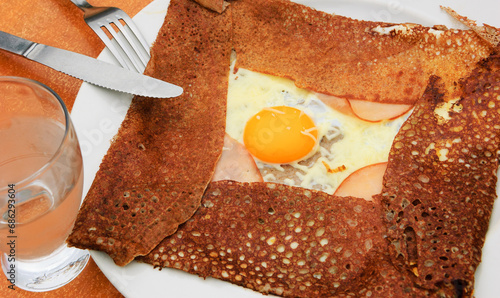 Galette complete. Traditional French buckwheat pancake with egg, cheese and ham served at typical Breton pancake restaurant (Creperie).
