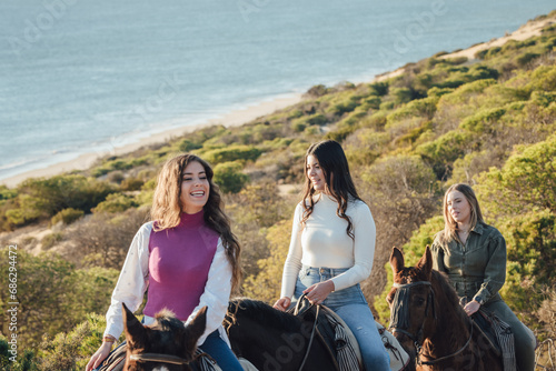 Cheerful female friends riding horses on hill near sea