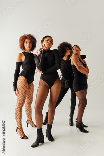 four appealing african american women in black alluring attire posing together, fashion concept
