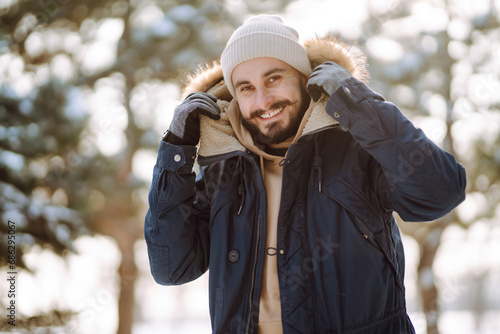 A young bearded man walks in a snowy park. Happy man enjoying the weather on a winter sunny day. Concept of walks, weekends. photo