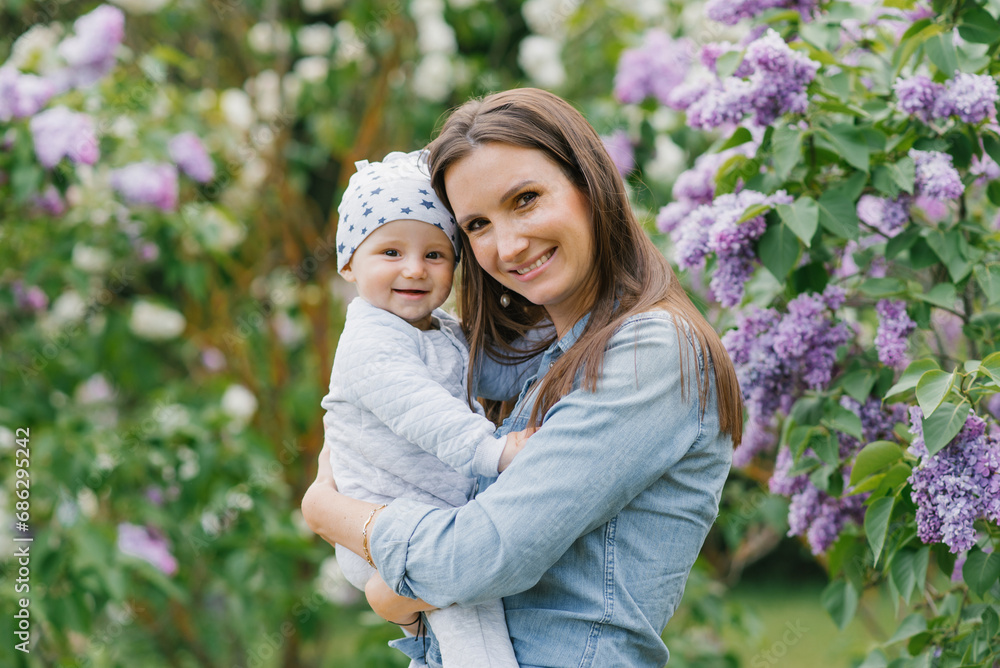 Young mother holds her baby son in her arms in a spring blooming lilac park