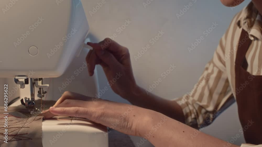 Tilt side shot of smiling Caucasian seamstress making red abstract seams on piece of cloth using sewing machine and enjoying it in atelier Tilt side shot of smiling Caucasian seamstress making red abstract seams on piece of cloth using sewing machine and enjoying it in atelier