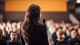 Back view of business woman female brunette long hair motivational speaker in front of her audience at a conference