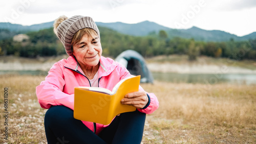 Happy senior woman reading a book outdoors during hiking day. Adventure and travel vacations concept #686311200