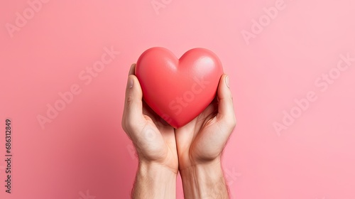 a man holds in his hands a model of a red heart on a pink background  the concept of love  mercy  medicine