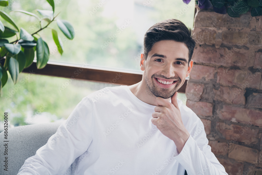 Photo of cheerful positive young guy wear white shirt sitting arm chair smiling indoors apartment room Photo of cheerful positive young guy wear white shirt sitting arm chair smiling indoors apartment room