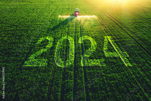 2024 Happy New Year concept and Aerial view of farming tractor plowing and spraying on field. © ValentinValkov
