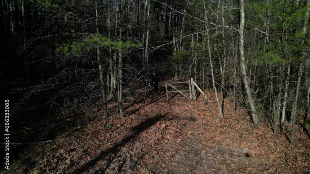 man walking his bicycle out of the woods past an abandoned fence gate made of wood and mounting the bike to ride away (cycling, biking, adventure, gravel, mountain, off road, woods, forest) man walking his bicycle out of the woods past an abandoned fence gate made of wood and mounting the bike to ride away (cycling, biking, adventure, gravel, mountain, off road, woods, forest)