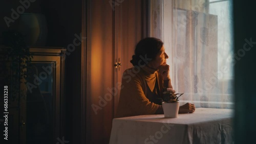 Thoughtful granny sitting at table, remembering past, looking out the window