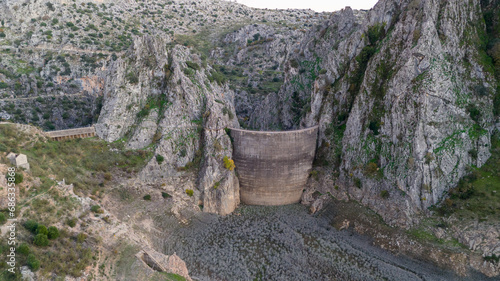 Stone dam of Montejaque, Spain in a rugged mountain landscape with sparse vegetation under a cloudy sky. photo