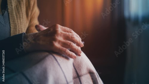 Senior woman covered in blanket sitting in armchair, close-up of trembling hands photo
