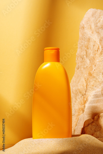 Bottle of sunscreen lotion and stone aagainst orange background photo