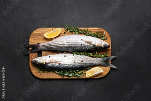 Raw grey mullet fish with spices and herbs in the cooking pan on black stone table top view. Raw fish ready to cook.