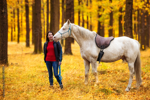 A pretty young woman and a white horse are in the autumn forest
