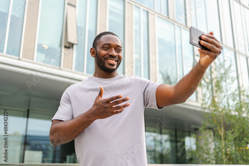 African American man holding smartphone having video chat on urban street in city. Guy blogger chatting with best friends in social network. Man having virtual meeting online chat video call outdoor © Юлия Завалишина