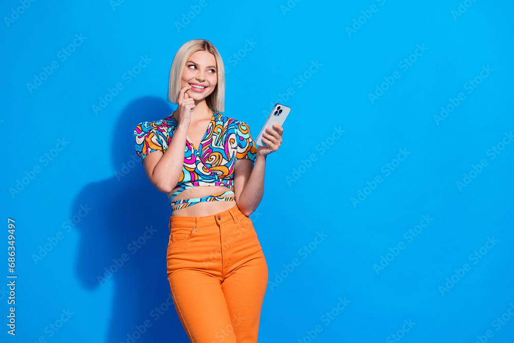 Portrait of creative lovely lady hold smart phone finger touch lips look empty space isolated on blue color background Portrait of creative lovely lady hold smart phone finger touch lips look empty space isolated on blue color background