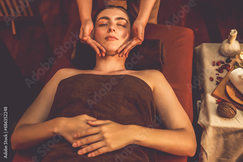 Caucasian woman enjoying relaxing anti-stress head massage and pampering facial beauty skin recreation leisure in warm candle lighting ambient salon spa in luxury resort or hotel. Quiescent