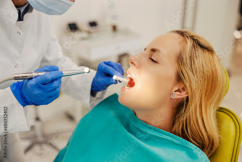Close up of woman with opened mouth at dentist office during tooth drilling procedure.