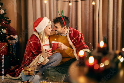 A happy couple is cheering with mugs while sitting at home on christmas and new year's eve.