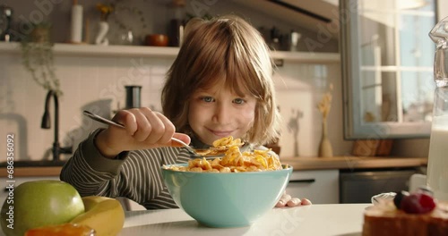 Adorable child eats cereal for breakfast at beautifully decorated table in modern kitchen. Advertising cinematic slow motion. Healthy children's traditional breakfast concept balanced food whole grain photo