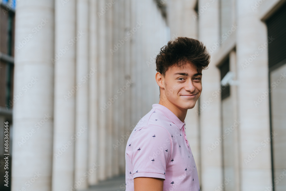 Cheerful boy standing against huge building with columns. Caucasian guy in pink polo looks at camera smiles enjoying life. Youth, carefree, freedom concept. Cheerful boy standing against huge building with columns. Caucasian guy in pink polo looks at camera smiles enjoying life. Youth, carefree, freedom concept.