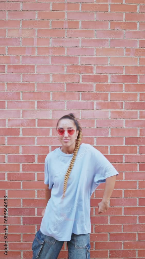 Vertical video of a young woman dancing popping against a brick wall in the city street. Active dancer performing hip hop with robotic moves in the street. Freestyle dancer. Vertical video of a young woman dancing popping against a brick wall in the city street. Active dancer performing hip hop with robotic moves in the street. Freestyle dancer.