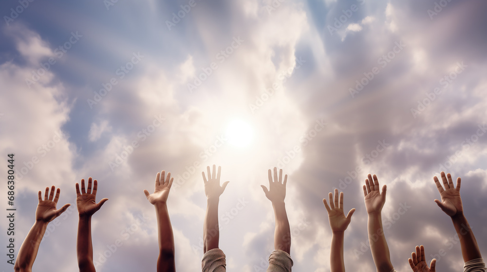 Many hands raised in the air in excitement, to support, pray, great, or show solidarity. Cheering people with raised arms, on sky background with sunlight and clouds. Copy space.