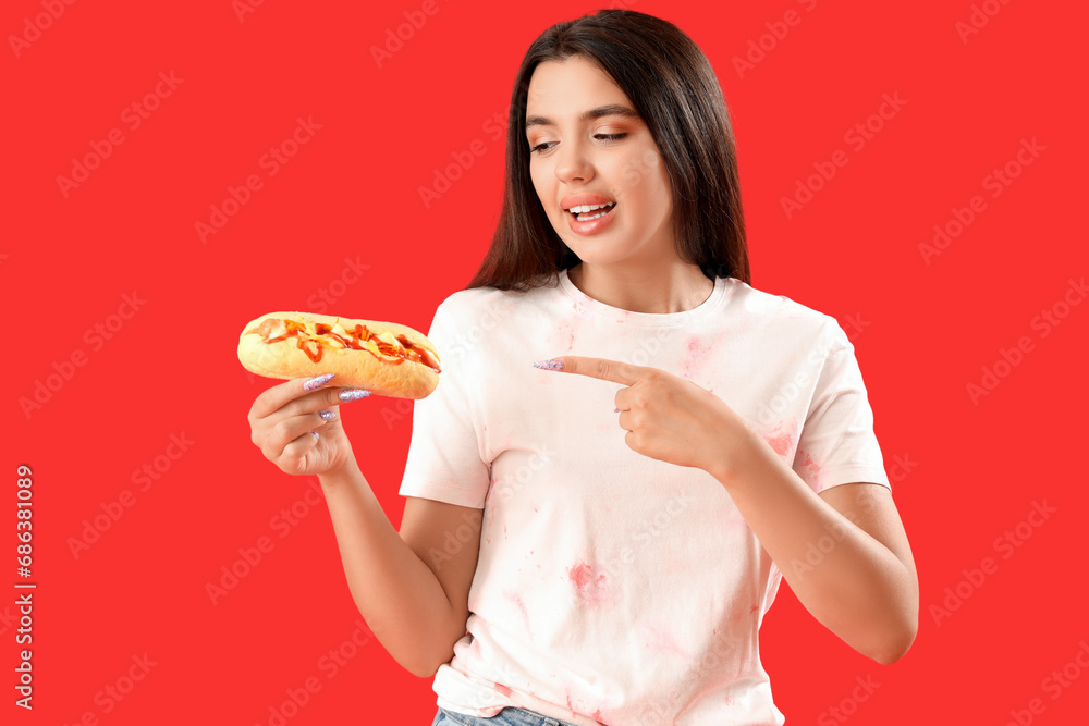 Pretty young woman pointing at tasty hot dog on red background Pretty young woman pointing at tasty hot dog on red background