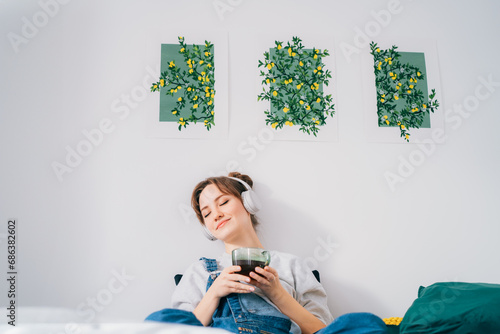 Woman with closed eyes listen music and enjoy cup of coffee or tea. Calm female spend free time at home enjoy favourite song with wireless modern headphones. Pastime weekend relax, no stress concept.