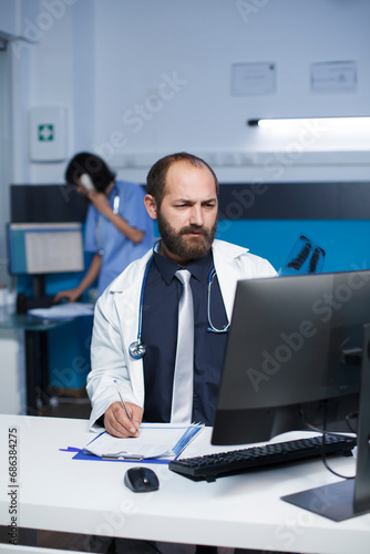 Selective focus on a white doctor studying a patient X-ray chest picture, and writing on his notepad. Close-up of a man with a lab coat, holding and examining a patient's chest scan.