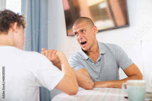 Young boy competing with his father in arm wrestling on kitchen table. photo