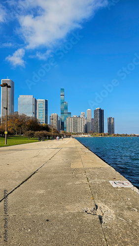 A beautiful autumn landscape at Lakefront Park with the rippling blue waters of Lake Michigan, autumn trees, people walking, skyscrapers and office buildings, blue sky and clouds in Chicago Illinoi photo