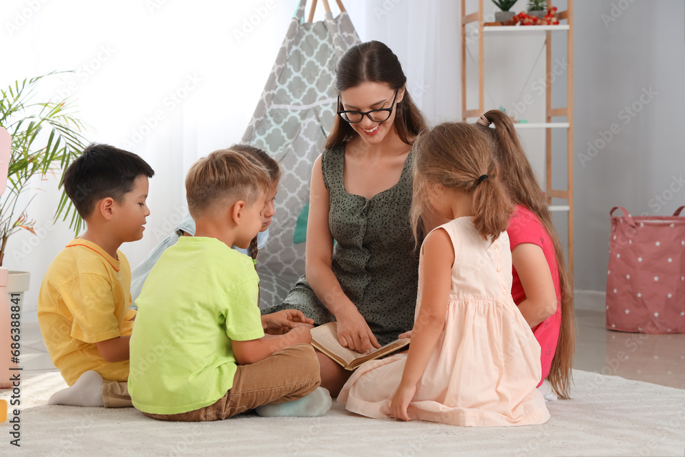 Nursery teacher reading story to little children in kindergarten Nursery teacher reading story to little children in kindergarten
