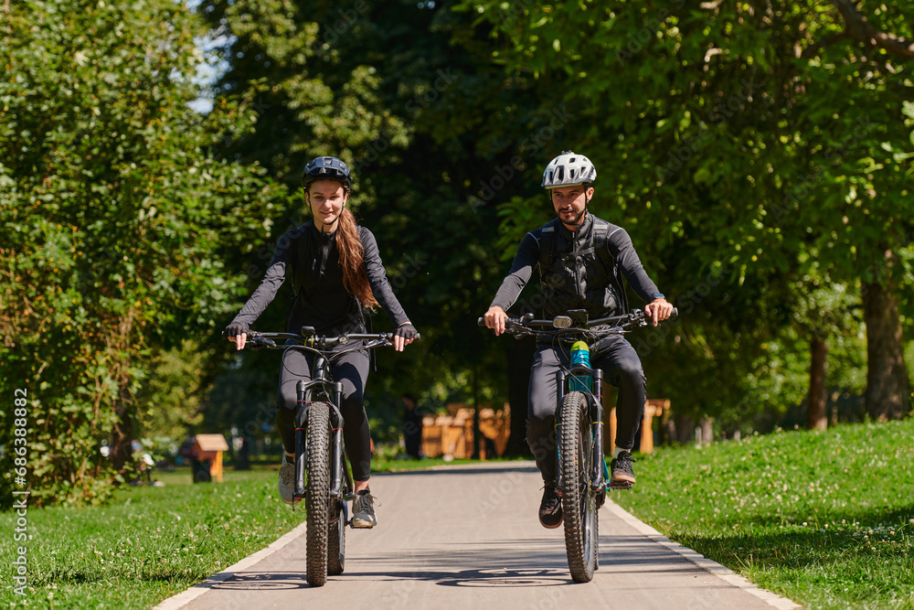 A blissful couple, adorned in professional cycling gear, enjoys a romantic bicycle ride through a park, surrounded by modern natural attractions, radiating love and happiness A blissful couple, adorned in professional cycling gear, enjoys a romantic bicycle ride through a park, surrounded by modern natural attractions, radiating love and happiness