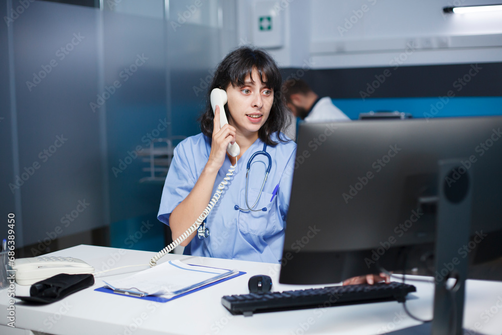 In the hospital office, a medical practitioner answers phones and schedules appointments. In a modern clinic, a health care provider sits at a desk, using a landline and staring at a monitor. In the hospital office, a medical practitioner answers phones and schedules appointments. In a modern clinic, a health care provider sits at a desk, using a landline and staring at a monitor.