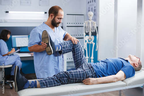 Cuadro en lienzo Physiotherapist performs leg exercise to stretch muscles and crack bones of elderly man in hospital cabinet