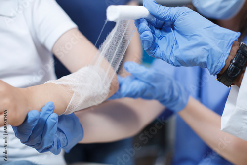 Close-up shot of a wound on the arm of a patient being carefully covered with a sterile dressing by multicultural medical professionals. Selective focus on a child being treated by a doctor and a photo