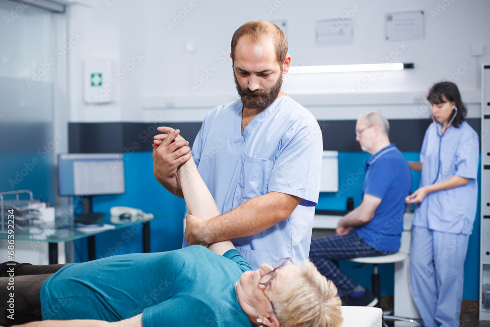 Elderly patient consults specialist assistant, receiving medical help for muscle pain. Nurse practitioner performs examination, stretches arms, and provides physiotherapy.