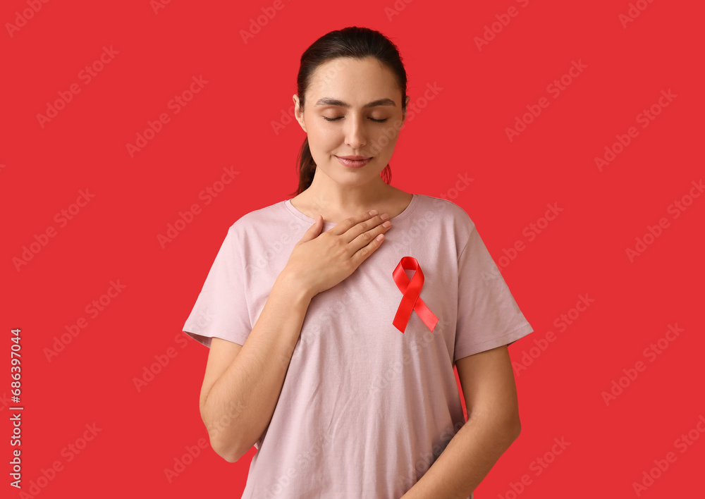 Young woman with red ribbon putting hand on heart against color background. AID awareness concept Young woman with red ribbon putting hand on heart against color background. AID awareness concept