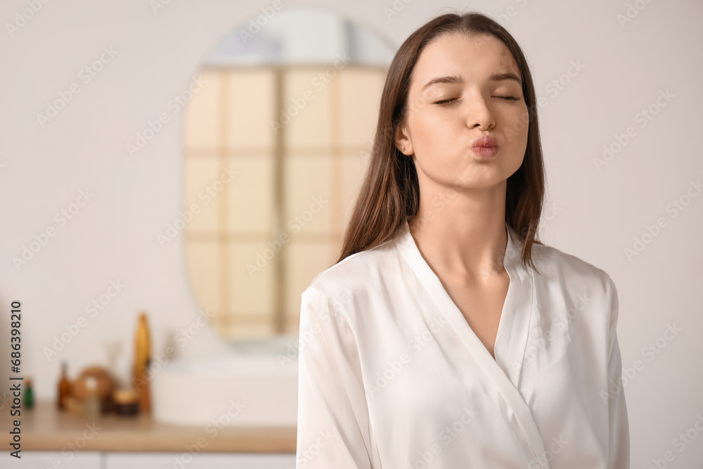 Young woman doing face building exercise in bathroom, closeup Young woman doing face building exercise in bathroom, closeup