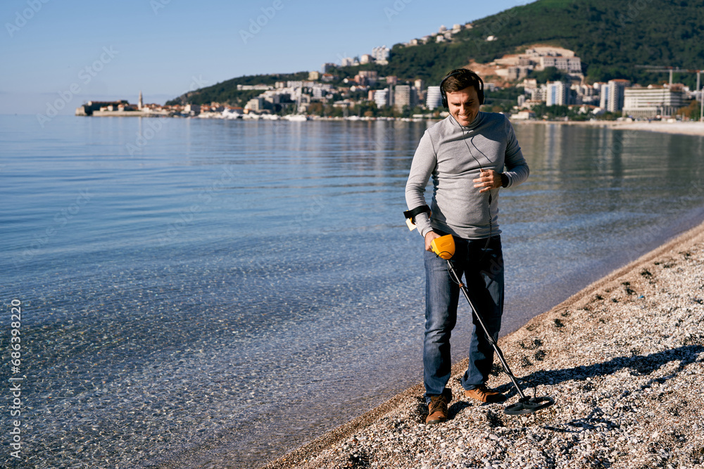 Man in headphones with a metal detector walks along the seashore