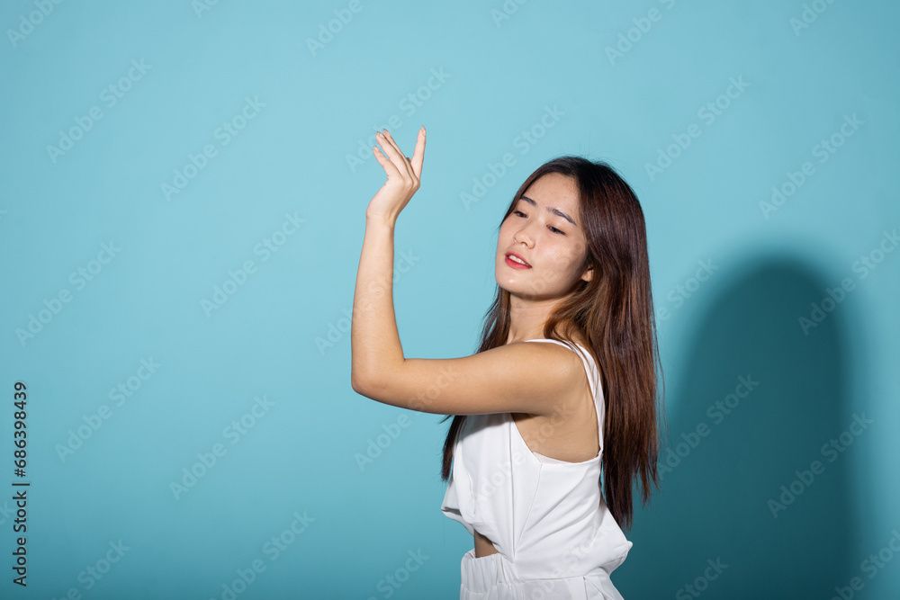 Fototapeta premium Asian young woman hand up cover face protect sun light and UV smile in studio shot isolated on blue background, female raising arm and hand in protection and block sunshine, sunscreen cream advertise